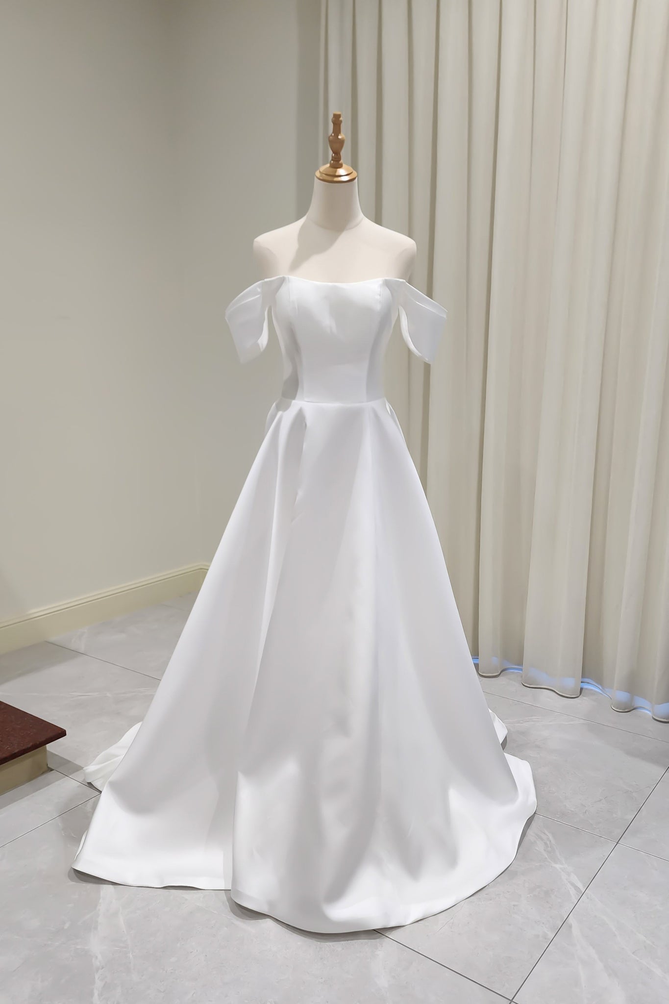White off-shoulder dress on a mannequin against a plain background