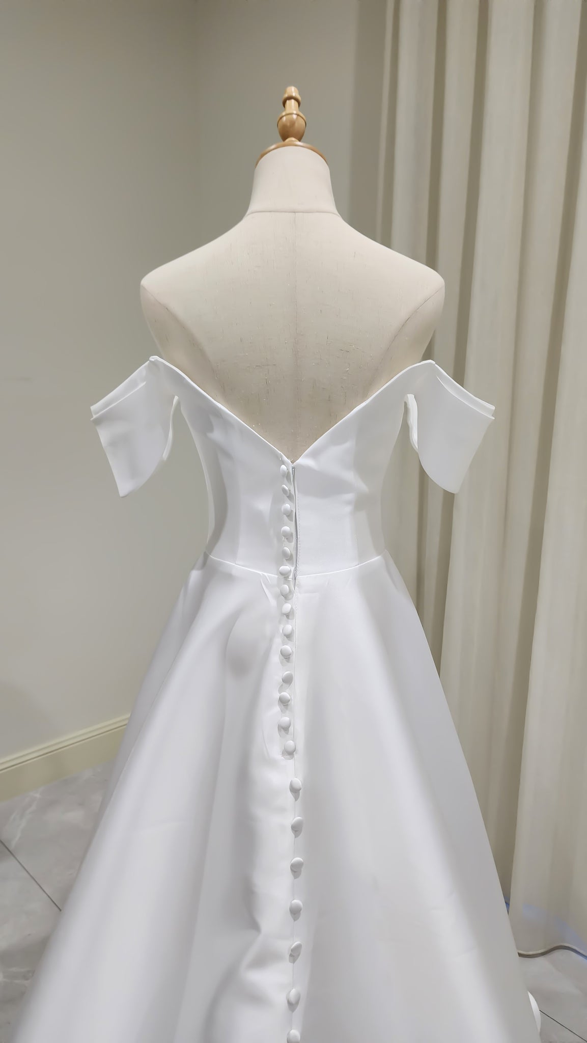 White off-shoulder dress on a mannequin against a neutral background